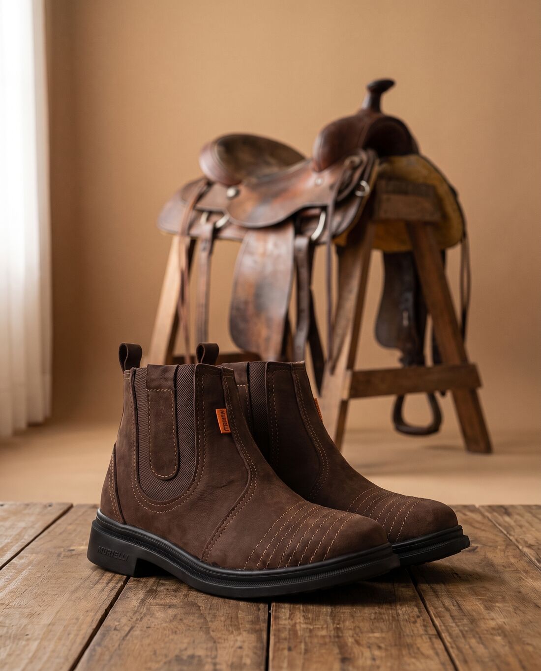 Par de botas Murielli Marrom ao lado de uma sela